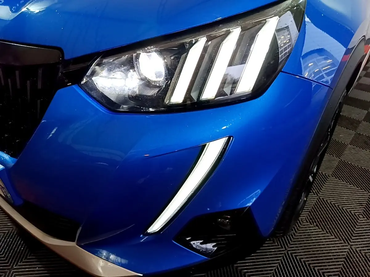 Gros plan sur l'avant droit bleu vif du Peugeot 2008 avec ses phares LED distinctifs en forme de griffes.
