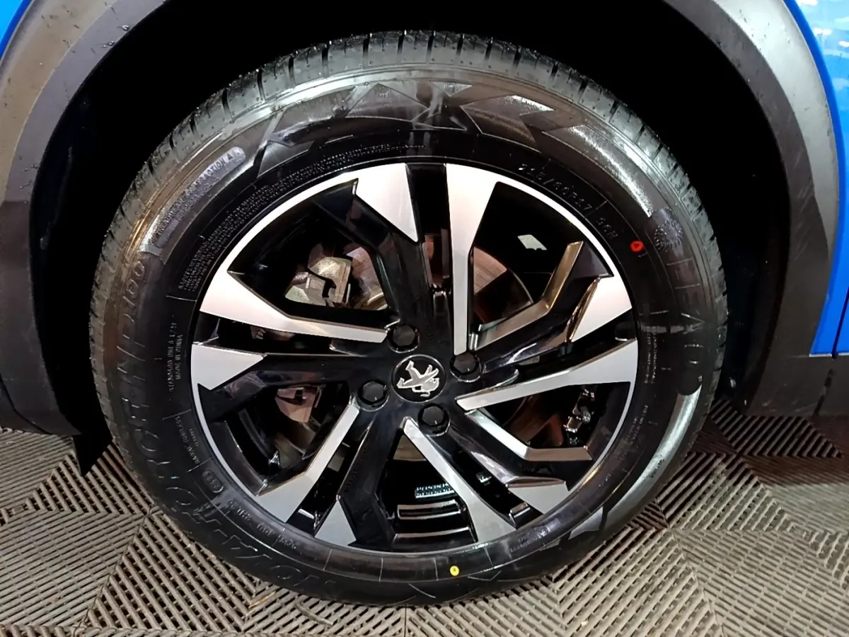 Gros plan sur la roue avant droite du Peugeot 2008 bleu, mettant en valeur la jante alliage bicolore au design moderne.