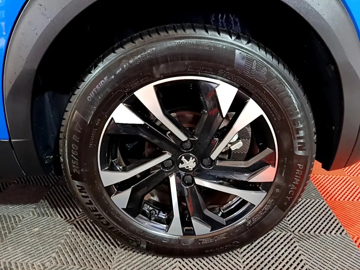 Gros plan sur la roue avant droite du Peugeot 2008 bleu, mettant en valeur la jante alliage noire et argentée.