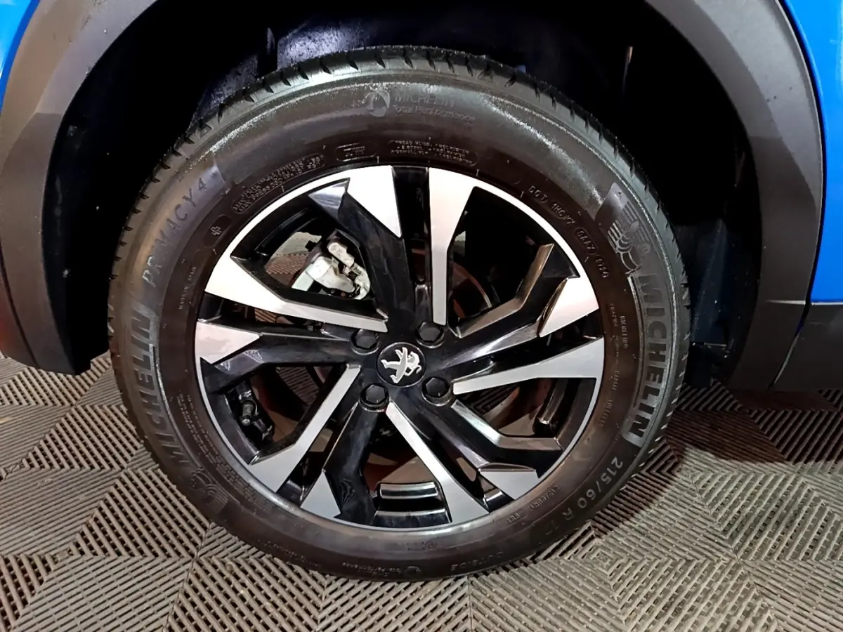 Gros plan sur la roue avant droite du Peugeot 2008 bleu, avec jante alliage bicolore et pneu Michelin.