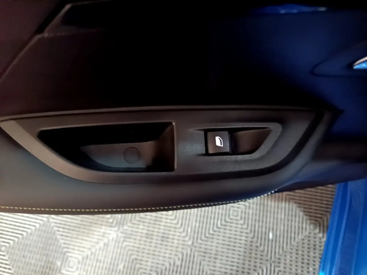 Gros plan sur la commande de lève-vitre côté gauche d’une Peugeot 2008 Bleu GT, avec couture blanche visible.