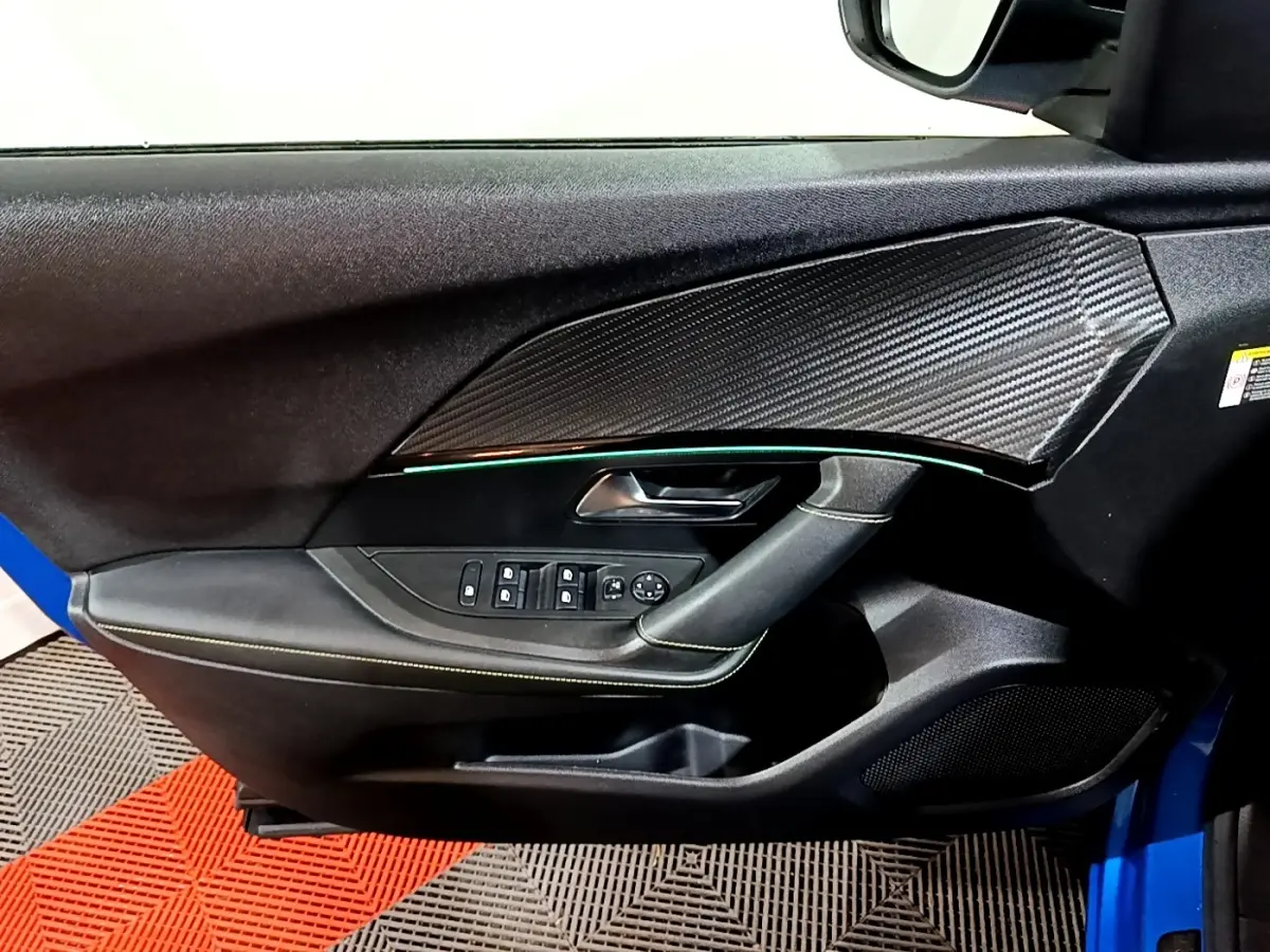 Vue intérieure côté gauche de la porte avant d’un Peugeot 2008 bleu avec insert effet carbone et éclairage d’ambiance vert.
