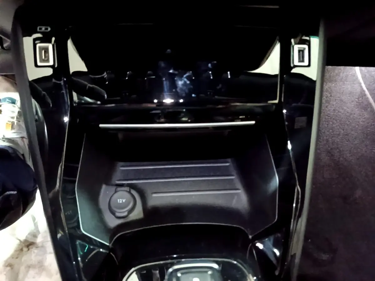 Vue rapprochée de la console centrale noire du Peugeot 2008 Bleu avec prise 12V visible au centre.