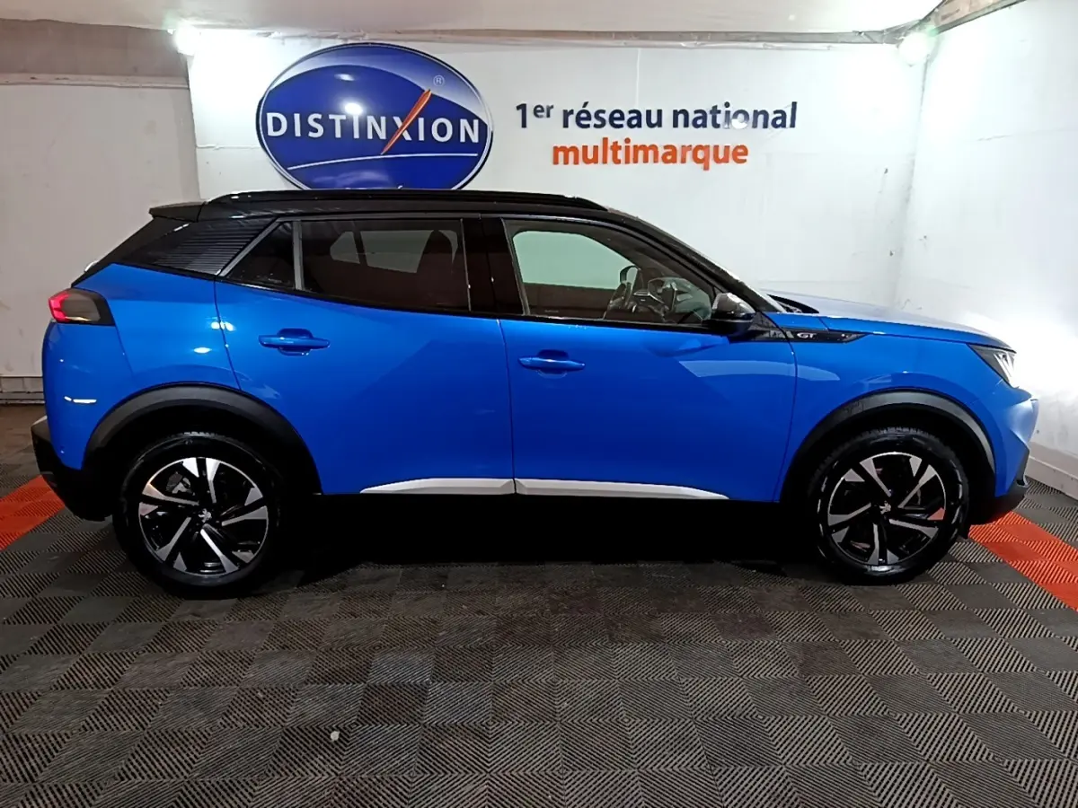 Vue de profil côté gauche d’un Peugeot 2008 GT bleu avec toit noir, roues alliage et logo GT sur l’aile avant.