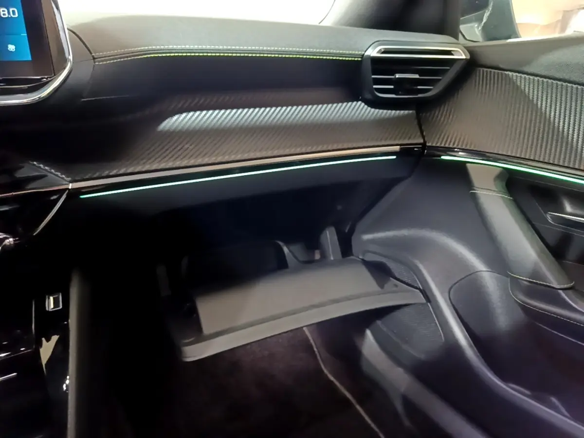 Intérieur de la Peugeot 2008 GT 2021, vue côté passager sur la boîte à gants ouverte et éclairage d’ambiance vert pâle.