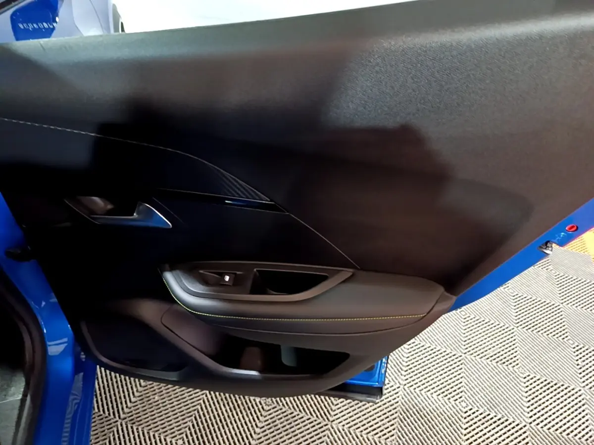Vue intérieure du panneau de porte côté gauche du Peugeot 2008 bleu, avec surpiqûres jaunes et poignée métallique.