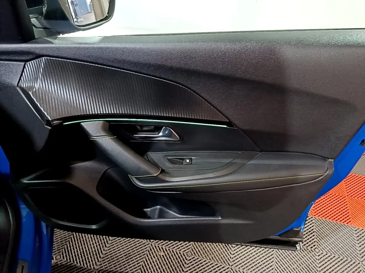 Vue intérieure de la porte avant gauche du Peugeot 2008 bleu, avec insert effet carbone et surpiqûres jaunes.