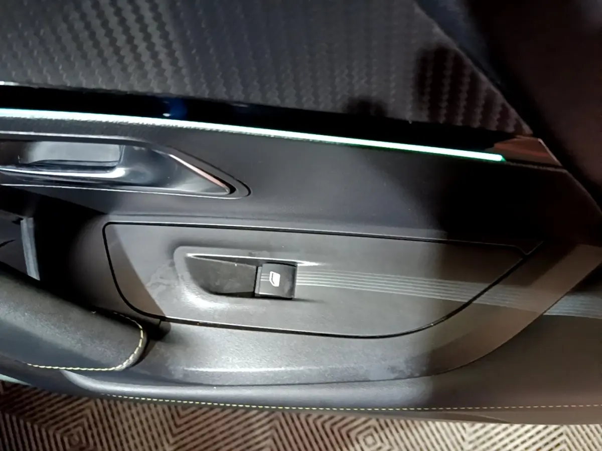 Gros plan sur la commande de lève-vitre côté gauche du Peugeot 2008 Bleu, avec insert décoratif et éclairage d’ambiance.