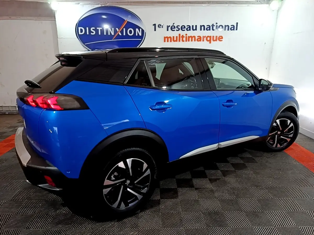 Vue 3/4 arrière droite d’un Peugeot 2008 GT bleu avec toit noir et feux arrière à griffes rouges allumés.