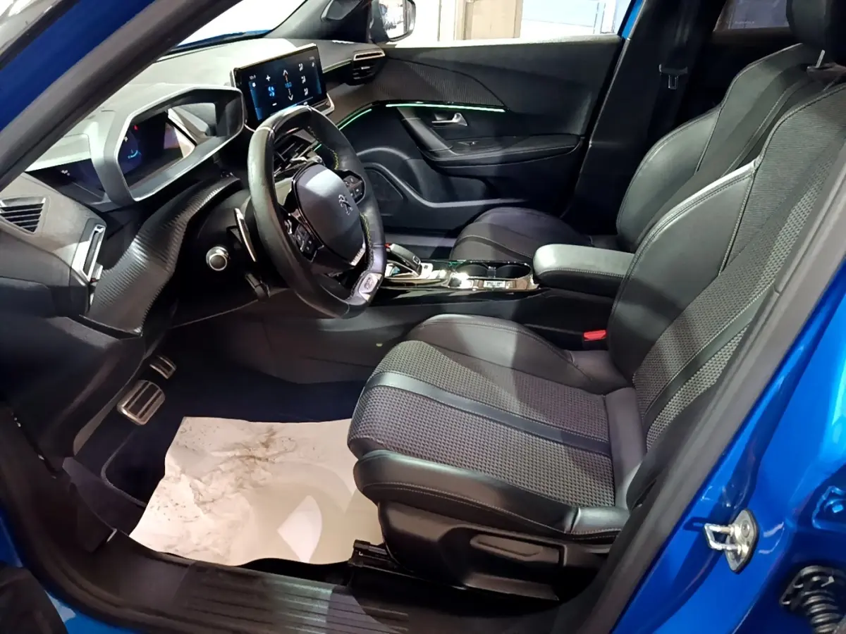 Vue intérieure côté conducteur du Peugeot 2008 bleu 2021, mettant en valeur le tableau de bord digital et les sièges en cuir noir.