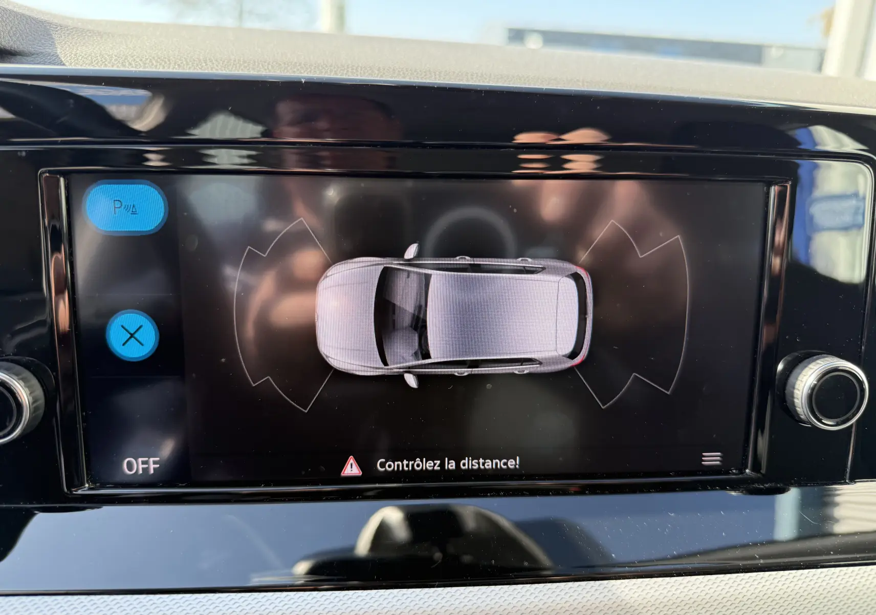 Écran de la console centrale affichant l'aide au stationnement avec vue aérienne du Volkswagen Golf blanc.