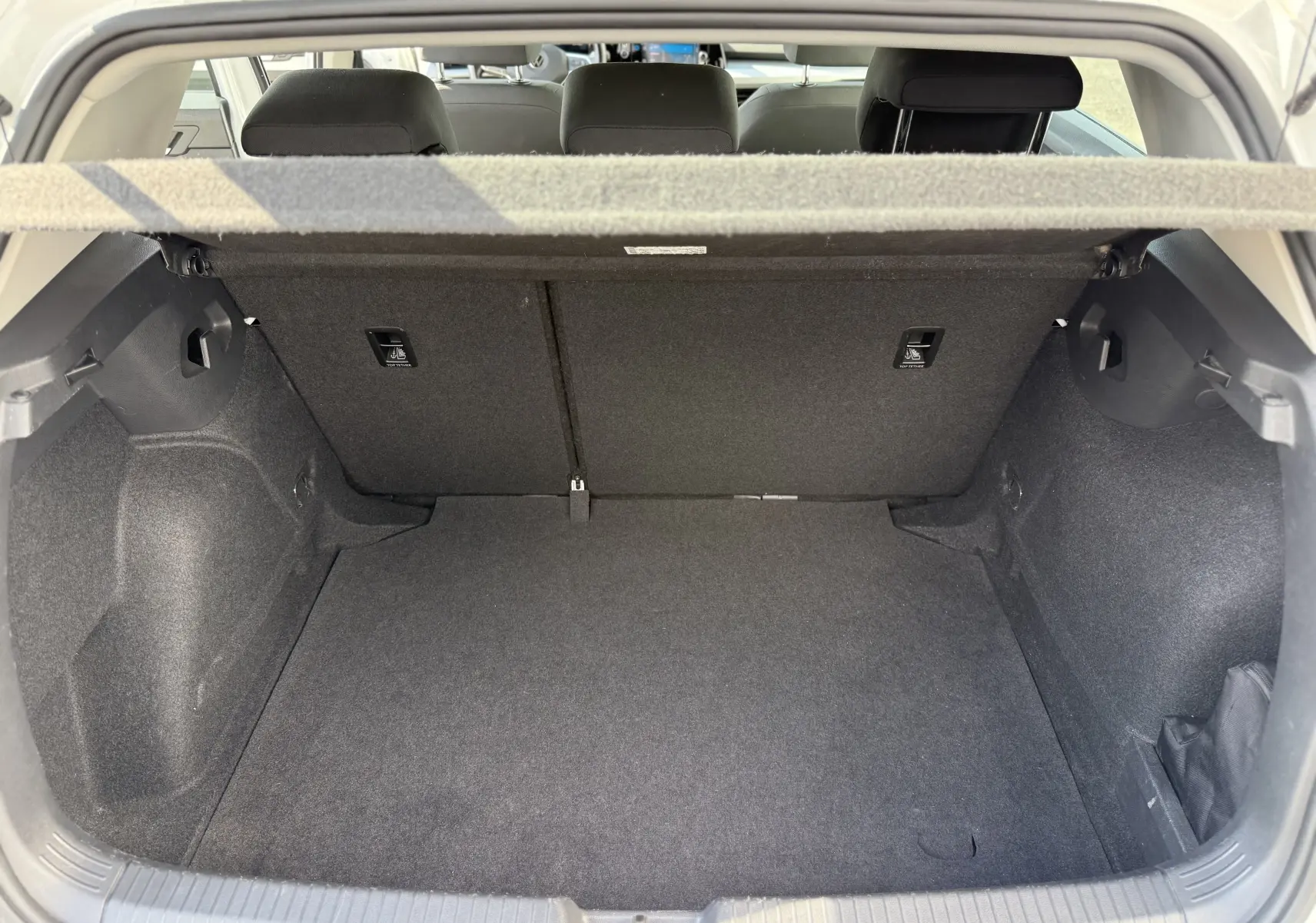 Coffre ouvert vu de l'arrière d'une Volkswagen Golf blanche 1.0 TSI 110 LIFE, intérieur noir et tapis de sol propre.