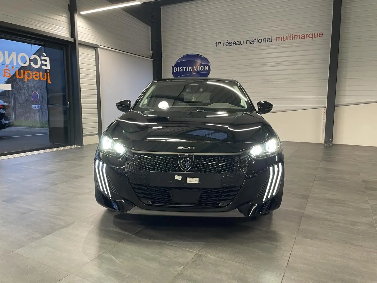 Vue avant d'une Peugeot 208 noire métallisée avec phares allumés et signature lumineuse en griffes LED.