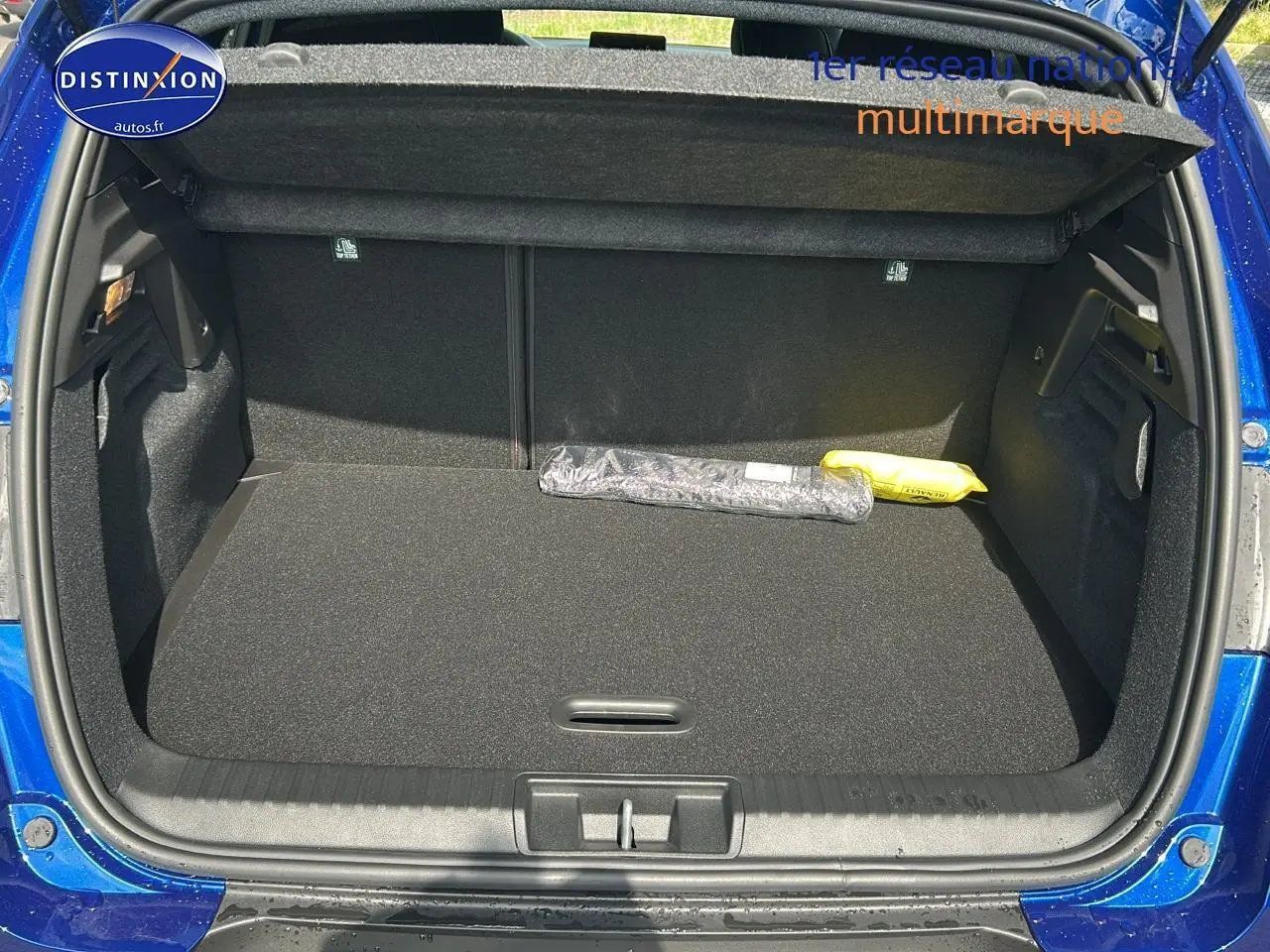 Coffre ouvert vu de l'arrière d'un Renault Captur 1.6 e-tech hybride 2025 bleu iron, avec tapis noir et objets posés.
