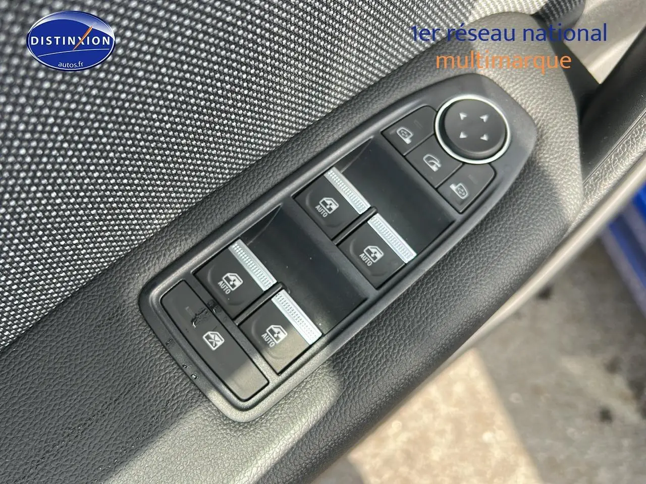 Gros plan sur les commandes des vitres électriques et rétroviseurs sur la porte avant gauche d'un Renault Captur bleu iron.