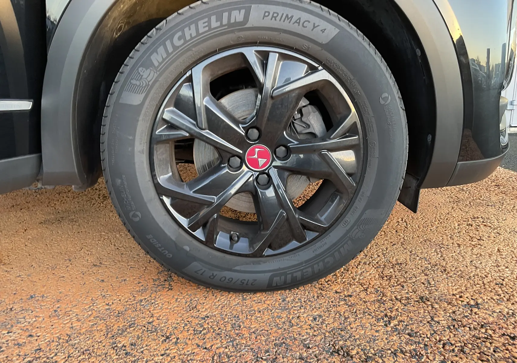 Gros plan sur la roue avant droite noire métallisée du DS3 Crossback 1.5 BlueHDi avec jante alliage noire et logo rouge central.