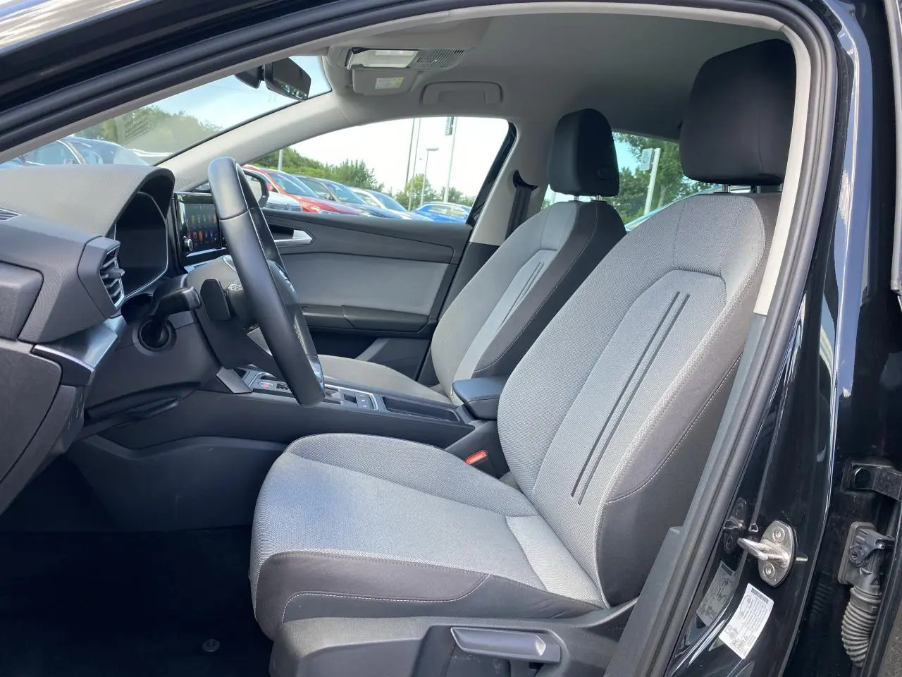 Intérieur côté conducteur d'une SEAT LEON 2024 noir Midnight, sièges tissu gris et tableau de bord moderne.
