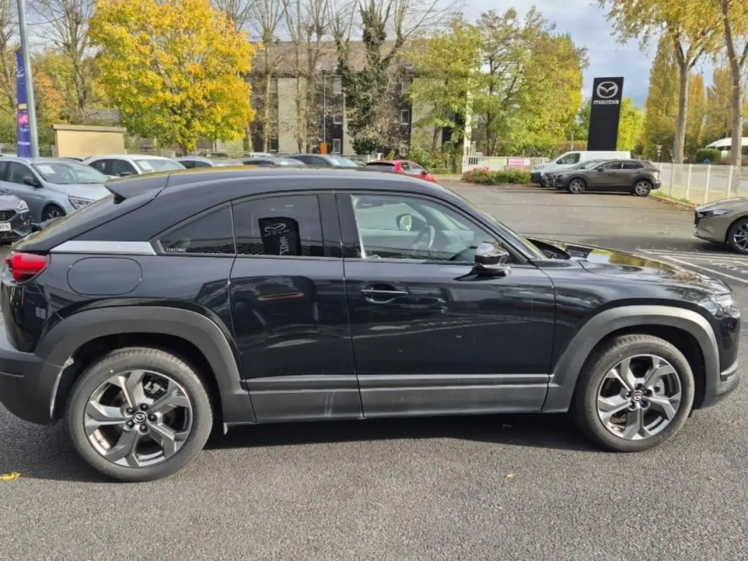 Vue de profil côté gauche d'un Mazda MX-30 électrique noir, avec jantes alliage et détails modernes en concession.
