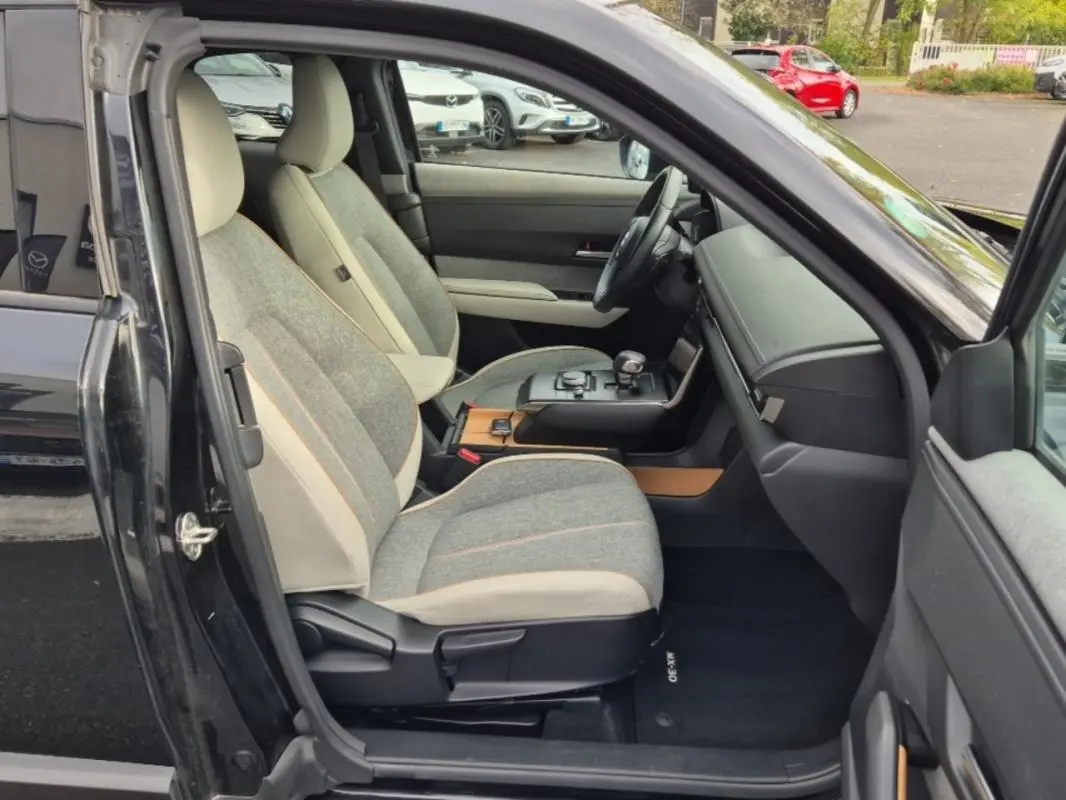 Vue intérieure côté conducteur du Mazda MX-30 2021, sellerie Modern Confidence gris clair avec inserts bois et tableau de bord noir.