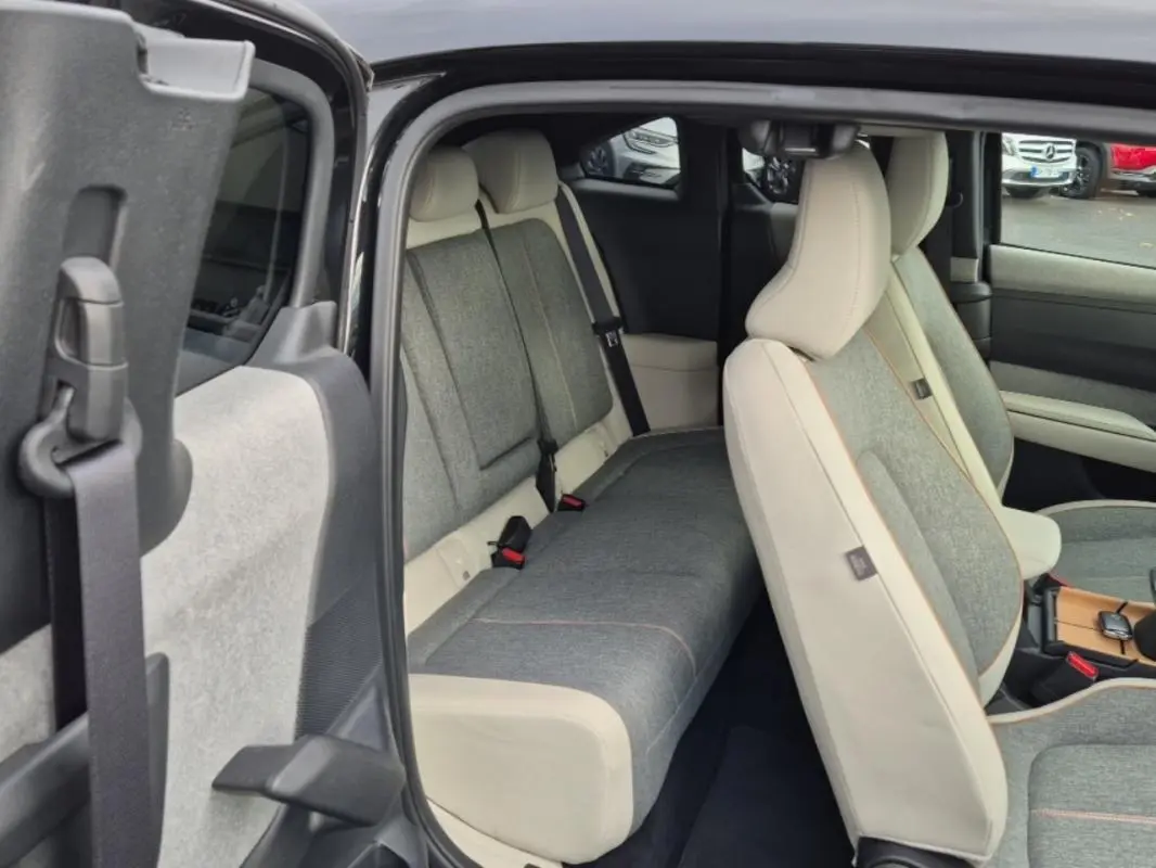 Intérieur de la Mazda MX-30 2021, vue côté gauche sur les sièges avant et arrière en tissu gris et cuir clair.