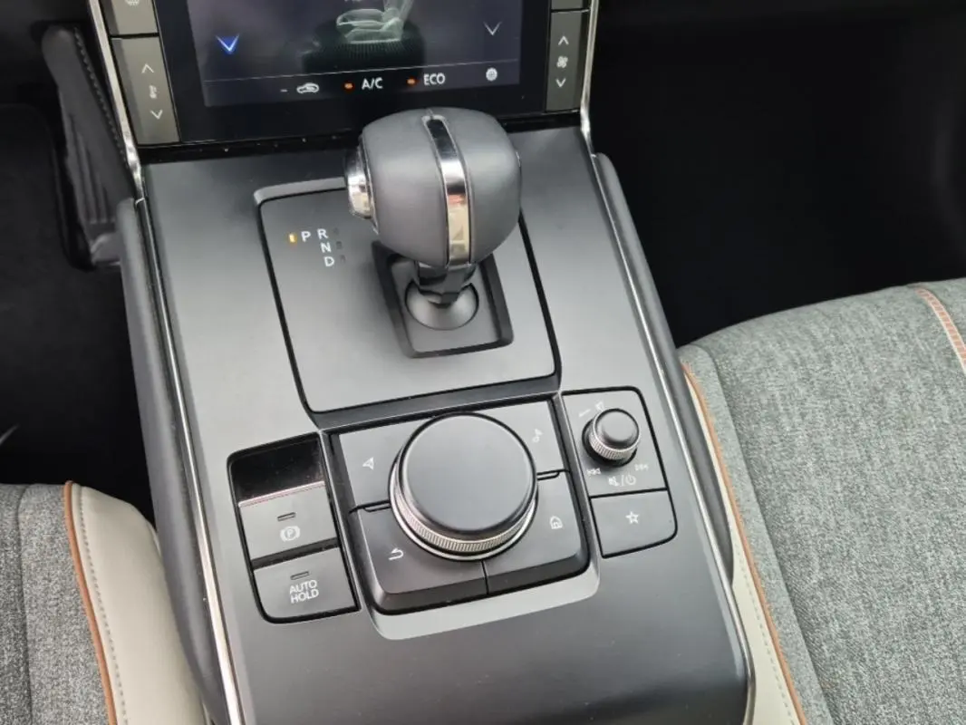 Gros plan sur la console centrale du Mazda MX-30 2021 électrique, avec levier de vitesse et molette de contrôle, sellerie grise.