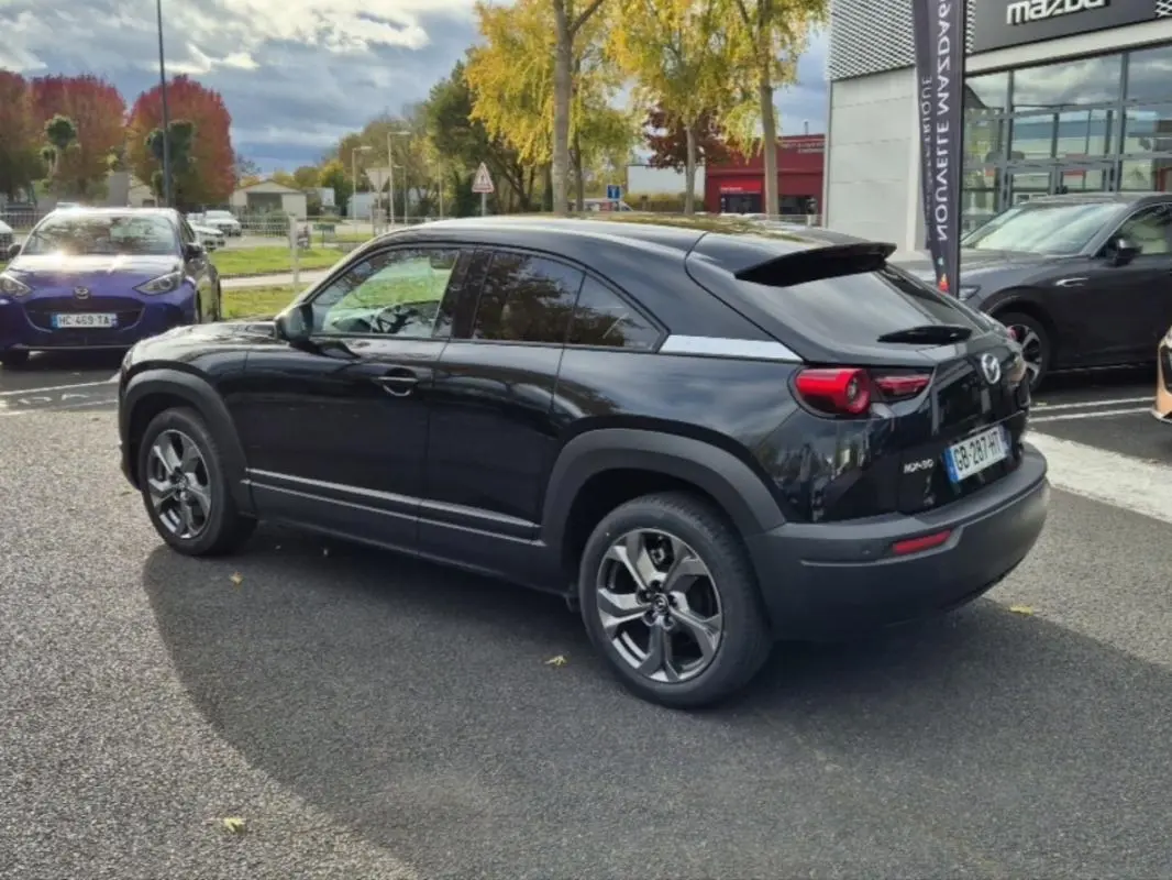 Vue 3/4 arrière droite d'un Mazda MX-30 électrique noir brillant, avec ses feux ronds distinctifs et jantes modernes.