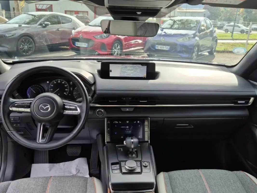 Intérieur de la Mazda MX-30 2021, vue de face sur le tableau de bord noir avec écran central et volant multifonction.
