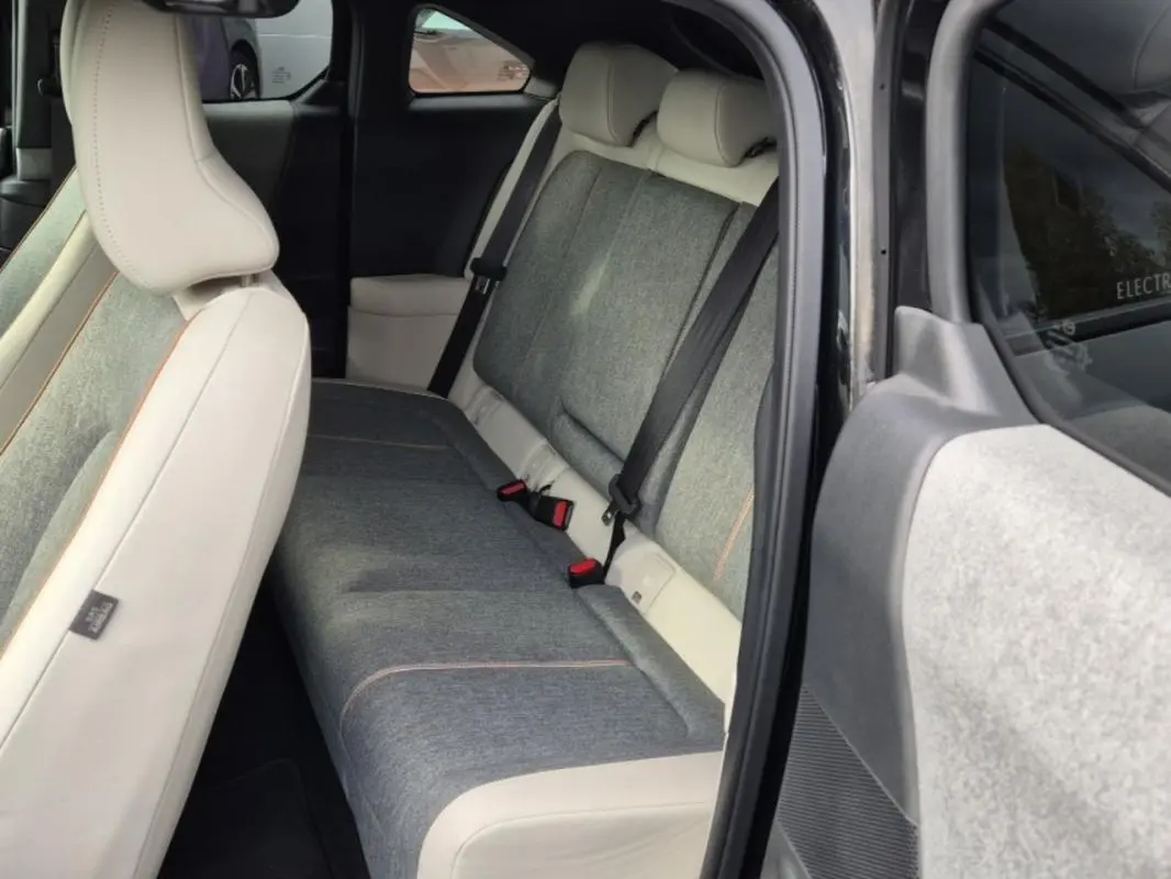 Vue intérieure arrière droite du Mazda MX-30 2021, sellerie moderne gris clair avec surpiqûres orange et ceintures noires.