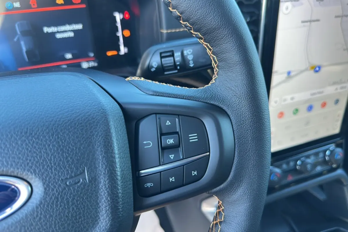 Gros plan sur le volant cuir noir avec surpiqûres jaunes du Ford Ranger Wildtrak Plus 2025 et son écran tactile GPS.