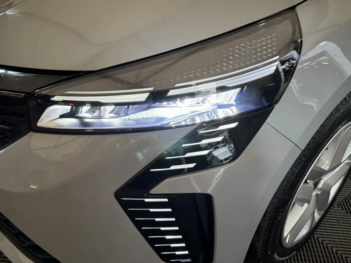 Gros plan sur le phare avant droit allumé de la Renault Clio gris clair Evolution Blue dCi 100 de 2025.