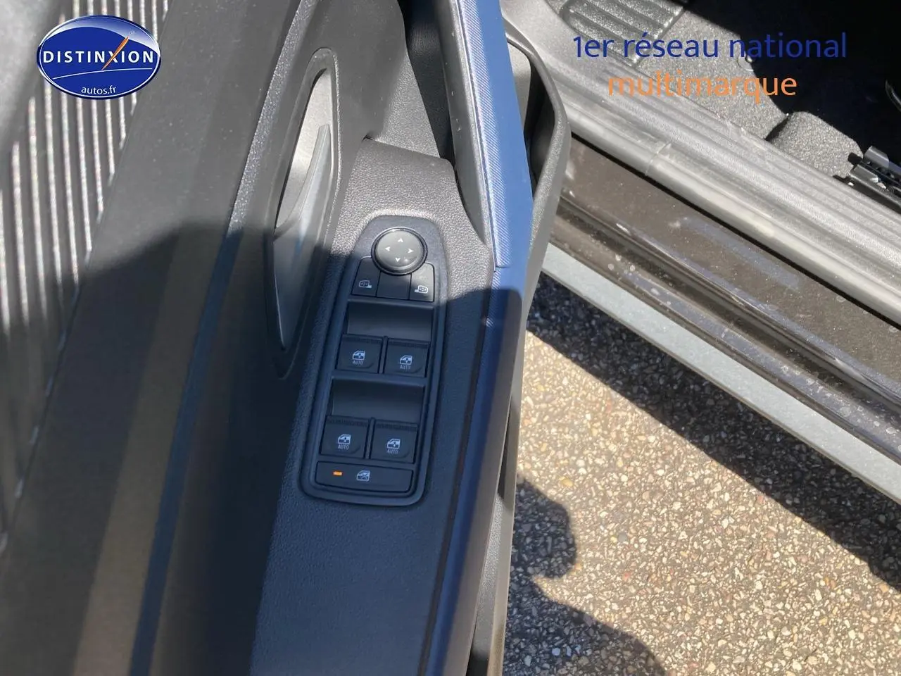 Vue rapprochée de la porte avant gauche du Dacia Duster noir, montrant les commandes électriques des vitres et le bouton de verrouillage.