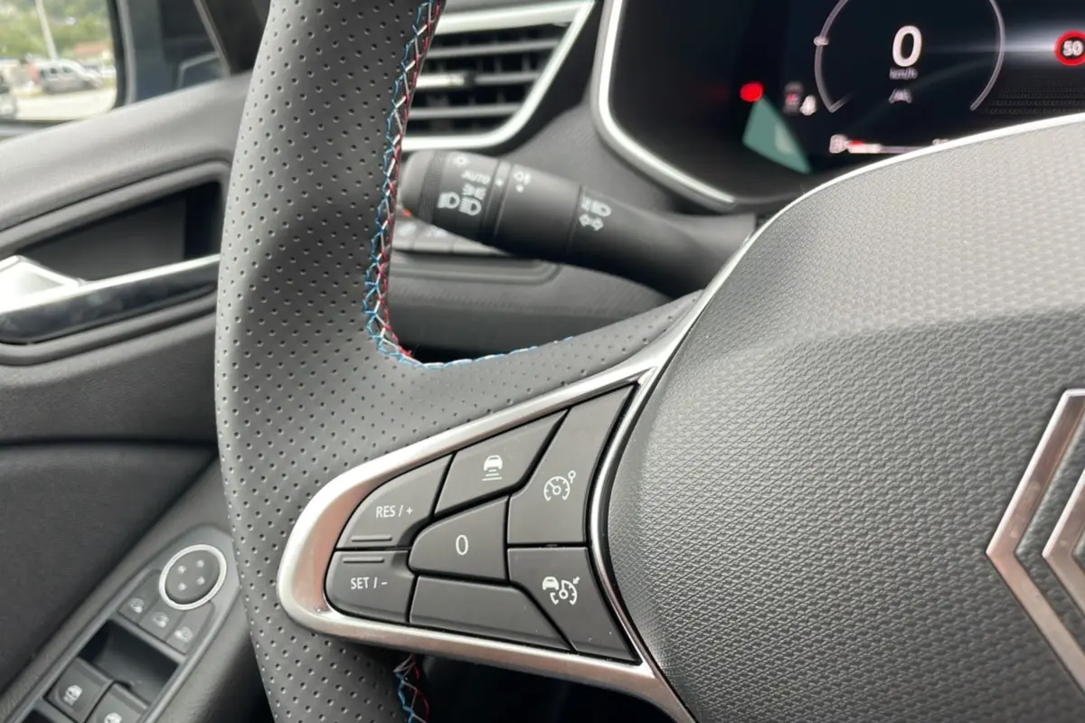Gros plan sur le volant perforé de la Renault Clio V TCE 90 Esprit Alpine 2025, avec surpiqûres tricolores et commandes intégrées.