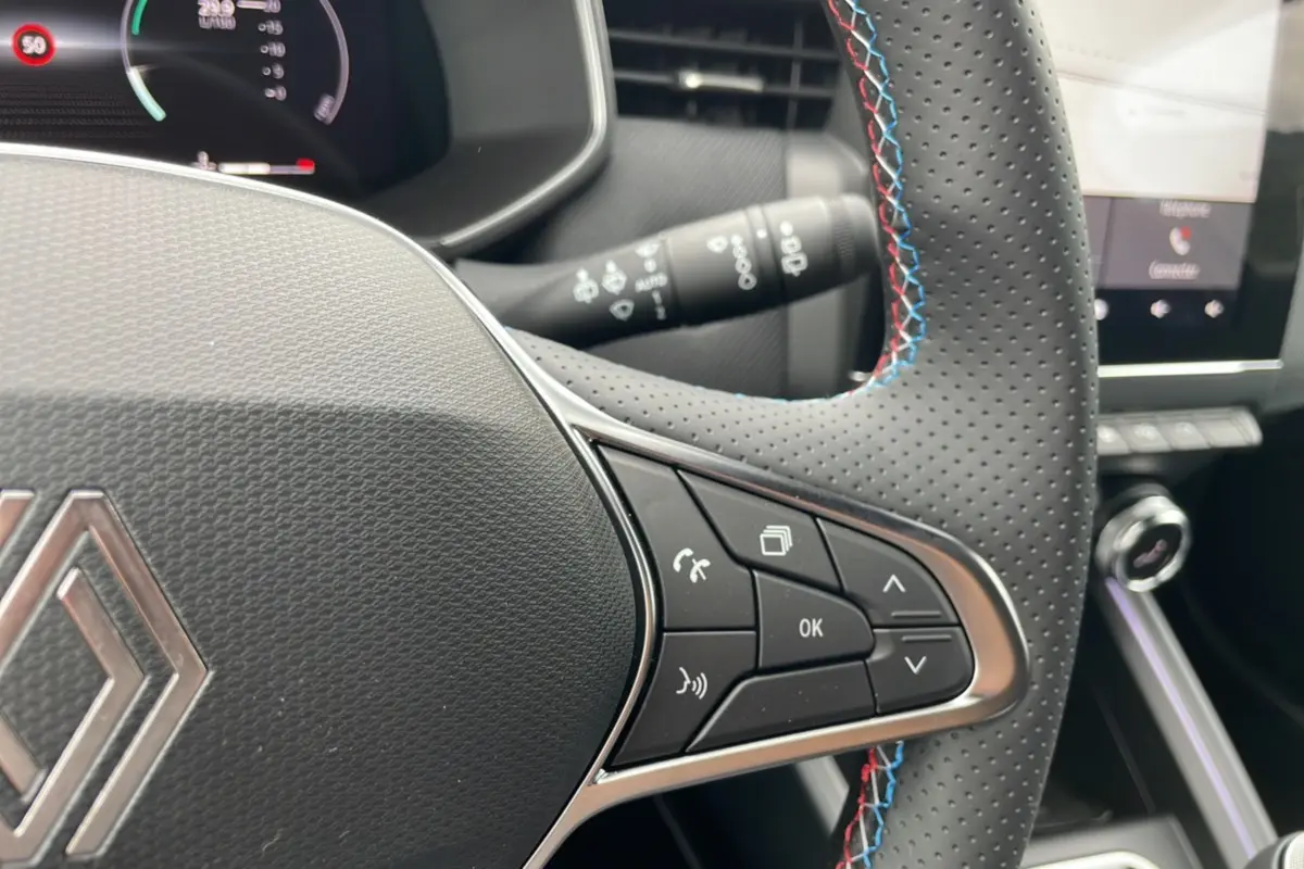 Gros plan sur le volant perforé de la Renault Clio V TCE 90 Esprit Alpine 2025 avec surpiqûres tricolores bleu, blanc, rouge.