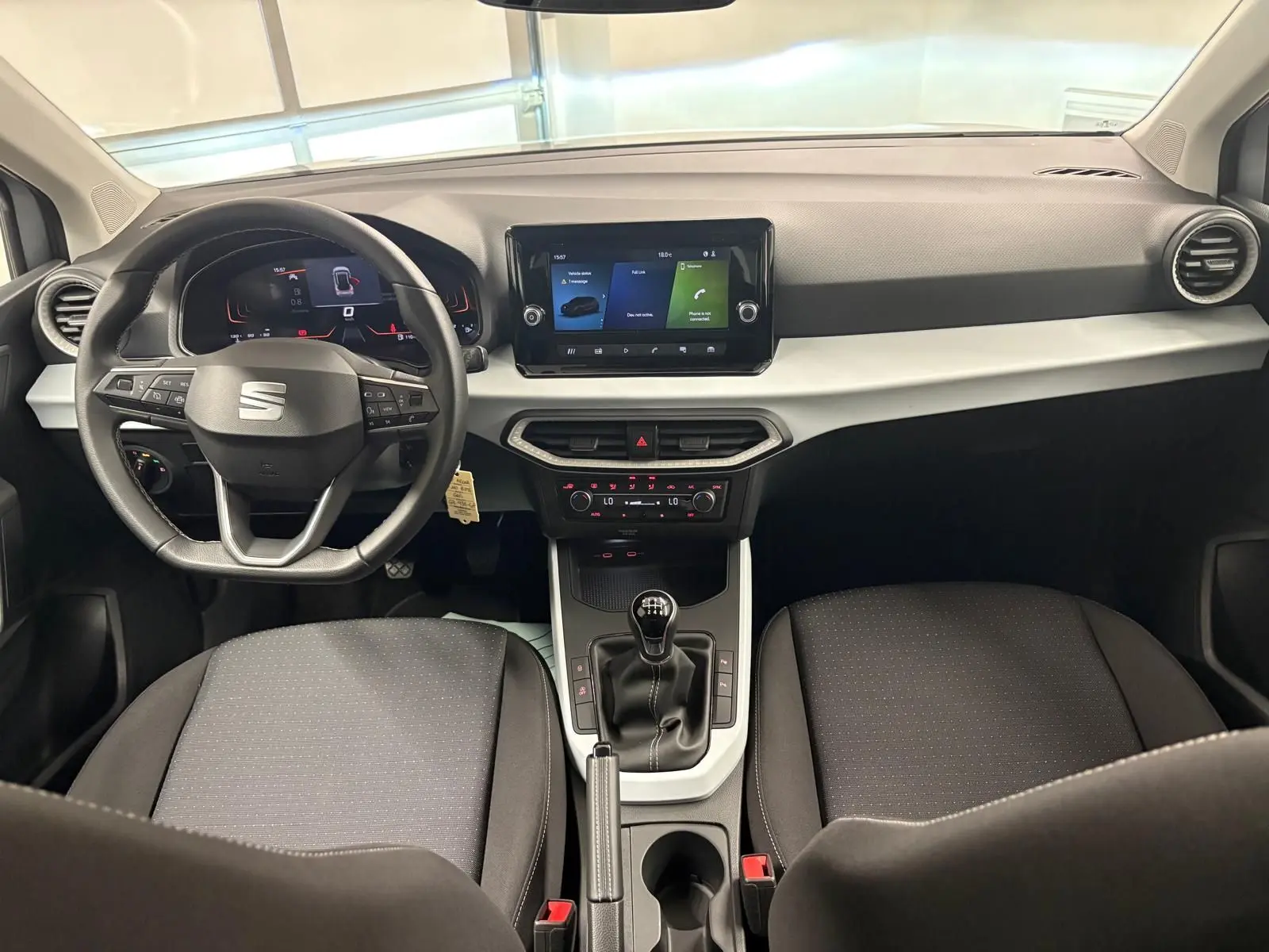 Intérieur avant du SEAT Arona 2024 avec tableau de bord moderne, écran tactile et boîte manuelle, sièges noirs.