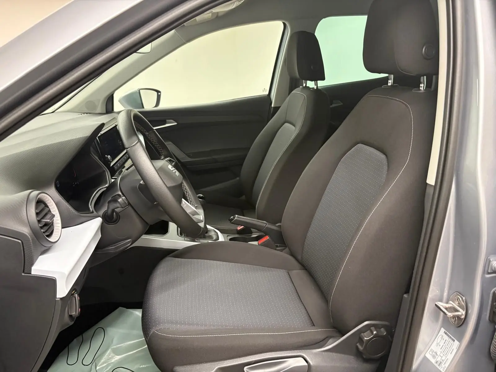 Vue intérieure côté conducteur du SEAT ARONA gris urbain 2024, sièges en tissu noir et tableau de bord moderne.