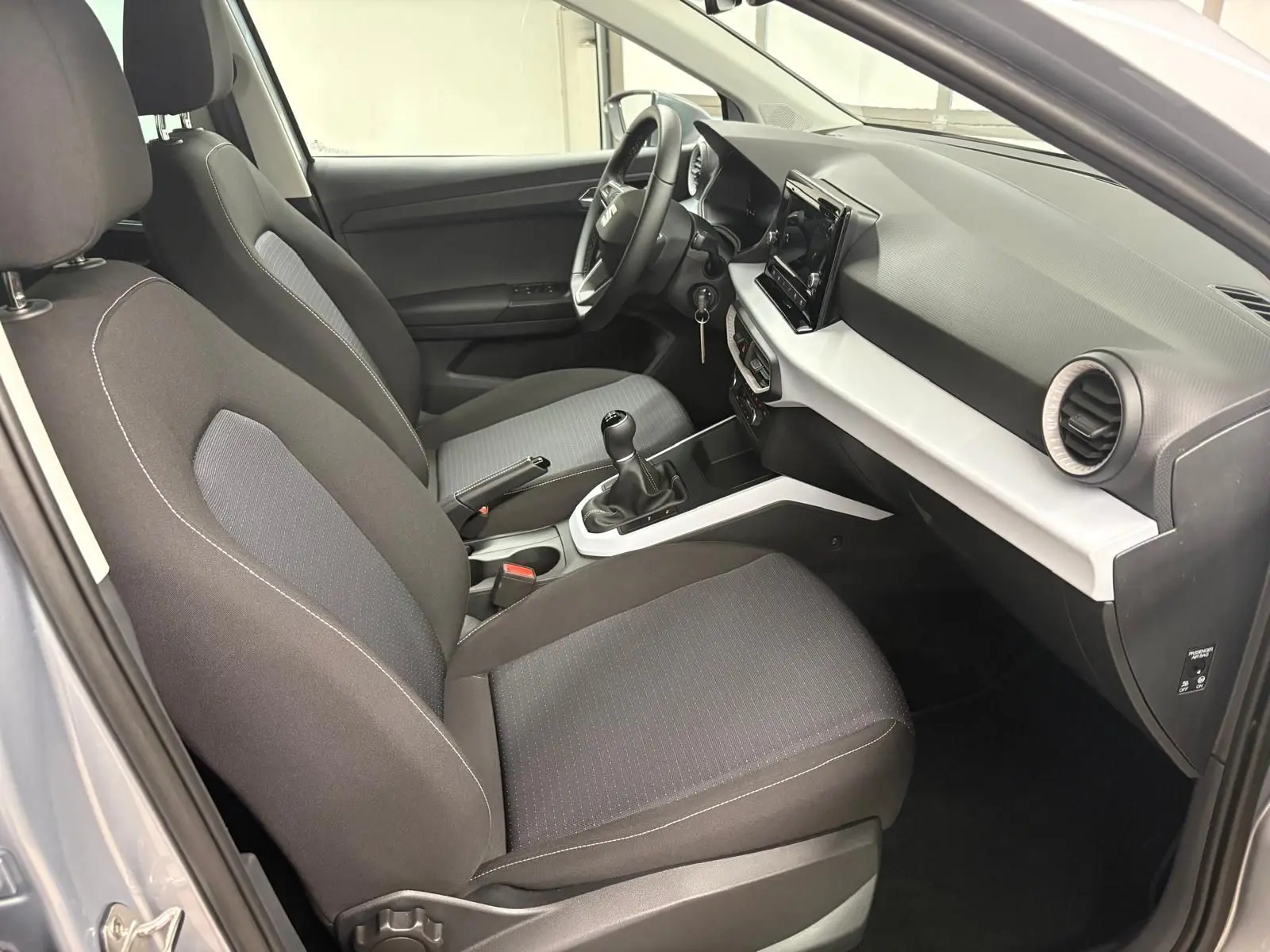 Intérieur avant droit du SEAT Arona 2024 gris urbain, sièges tissu noirs et console centrale avec boîte manuelle.