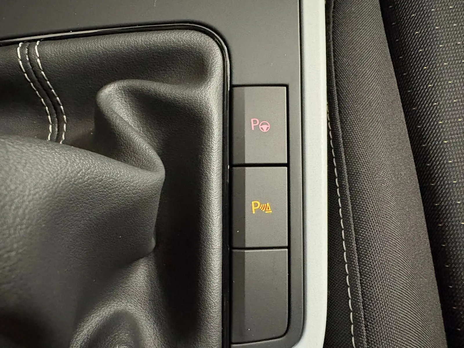 Gros plan sur la console centrale du SEAT Arona 2024 montrant le soufflet de levier de vitesses et les boutons d'aide au stationnement.