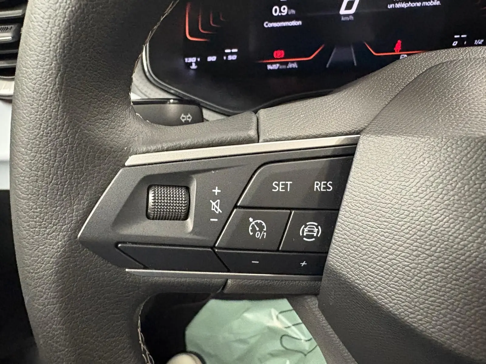 Gros plan sur les commandes du volant gauche du SEAT Arona 2024 gris urbain, avec régulateur de vitesse et volume.