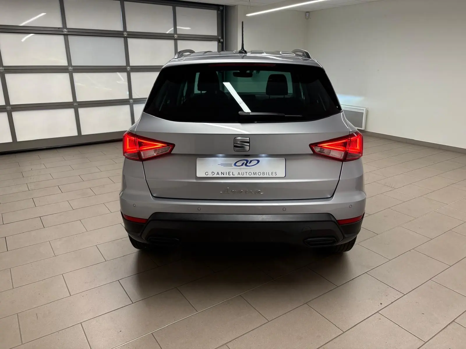 Vue arrière d'un SEAT Arona 2024 gris urbain avec vitres surteintées et feux arrière allumés dans un garage.