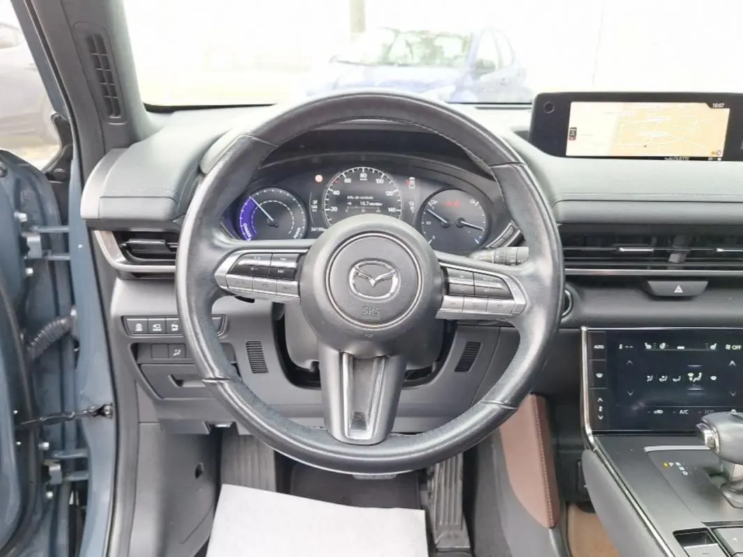 Vue intérieure centrée sur le volant noir du Mazda MX-30 gris, avec tableau de bord numérique et écran tactile visible.
