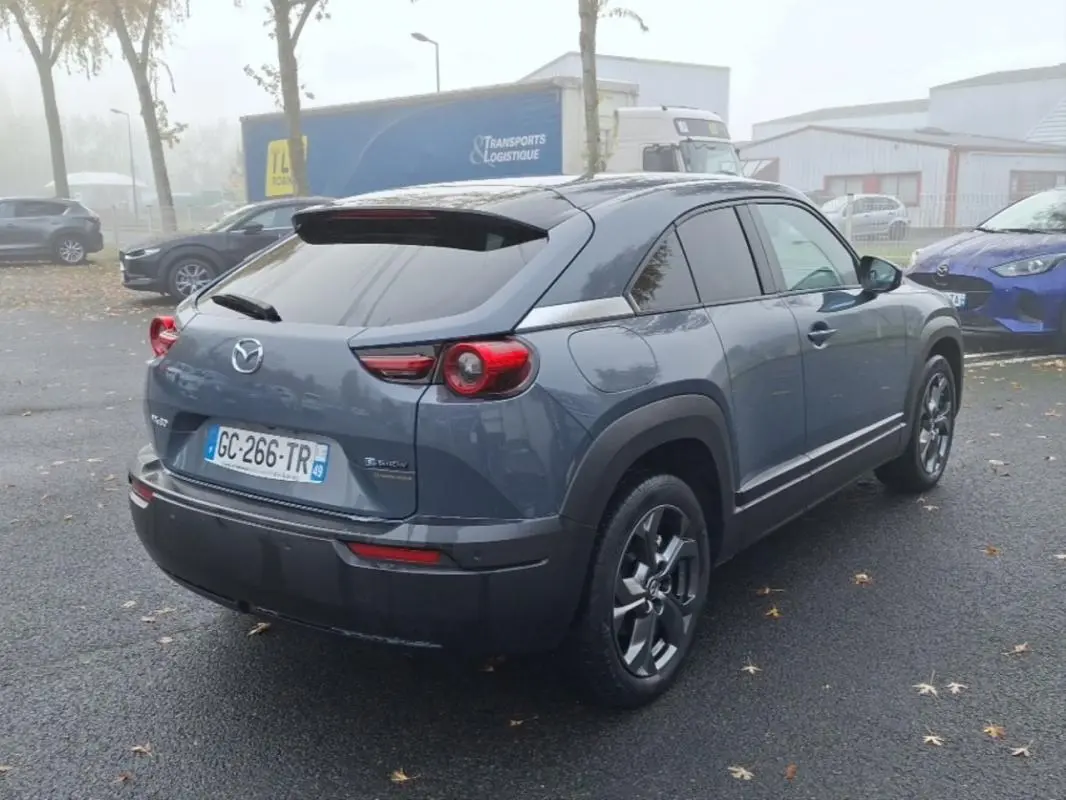 Vue 3/4 arrière droite d'un Mazda MX-30 gris électrique 2021 avec feux arrière ronds et jantes foncées.