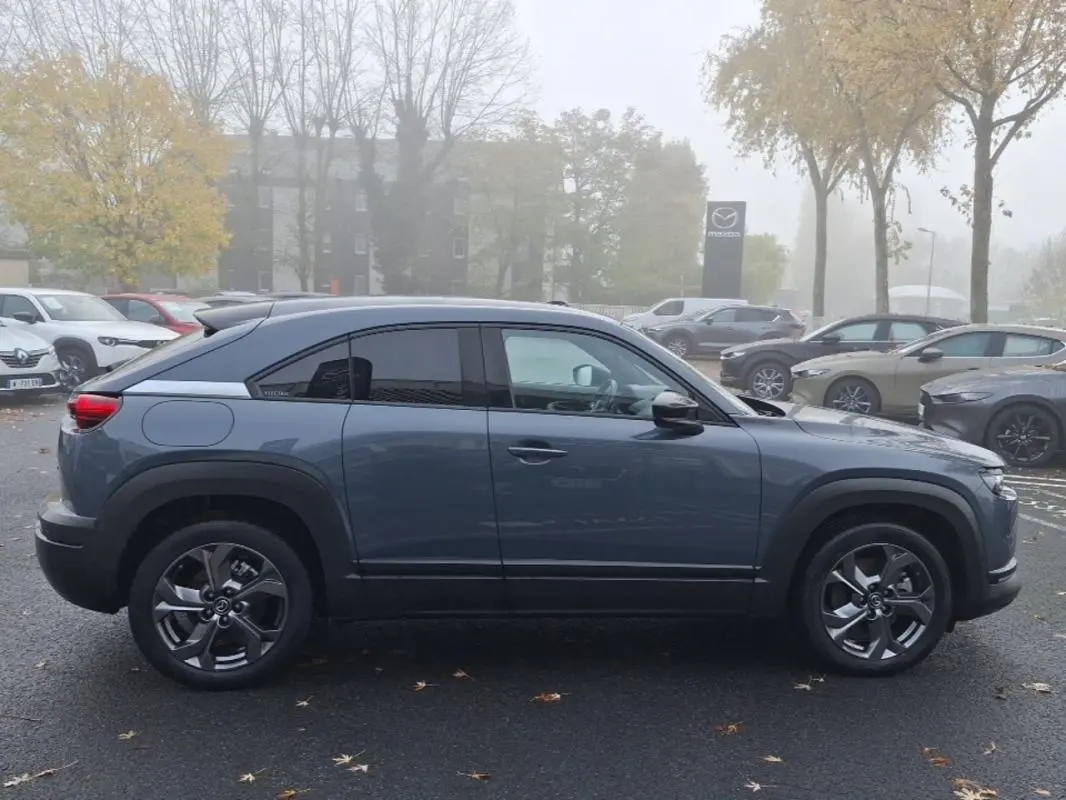 Vue de profil côté gauche d’un Mazda MX-30 gris électrique 2021 avec jantes spécifiques et toit noir contrasté.