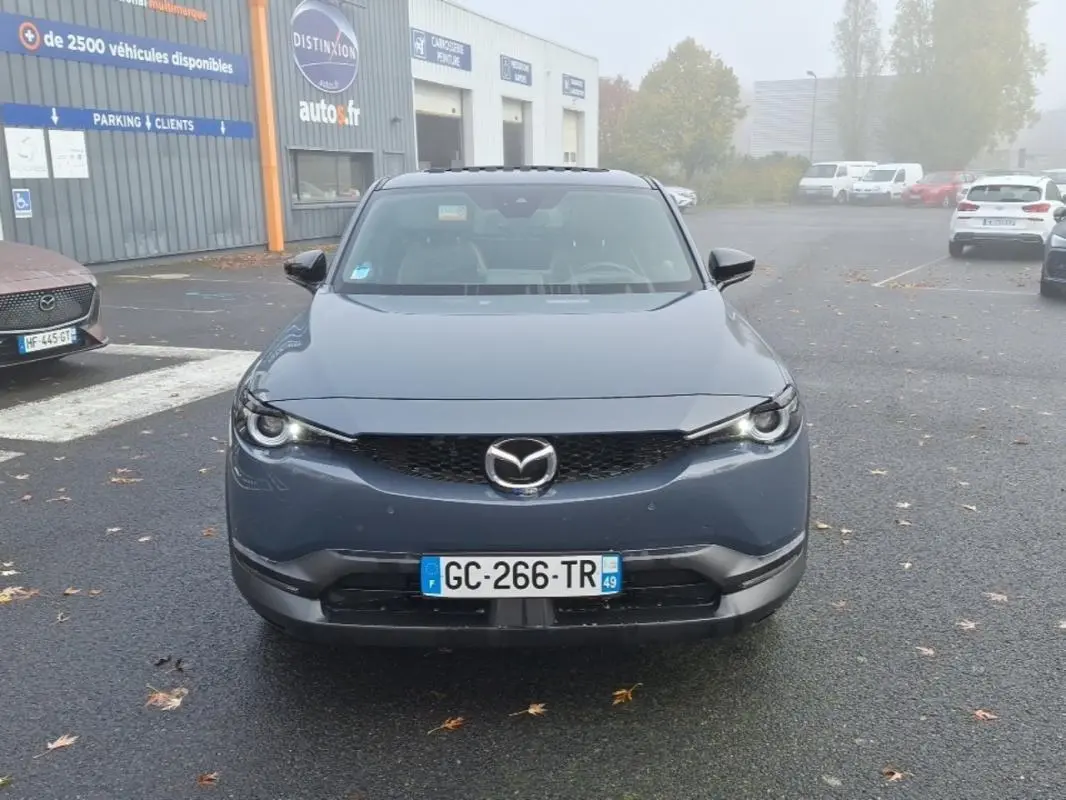 Vue frontale d'un Mazda MX-30 gris électrique 2021, avec calandre noire et phares LED allumés.
