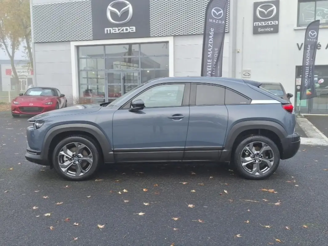 Vue de profil côté gauche d'un Mazda MX-30 gris électrique 2021 devant une concession Mazda.