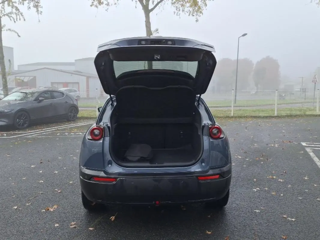 Vue arrière de la Mazda MX-30 gris 2021 avec coffre ouvert, montrant l'espace de chargement vide sur un parking extérieur.