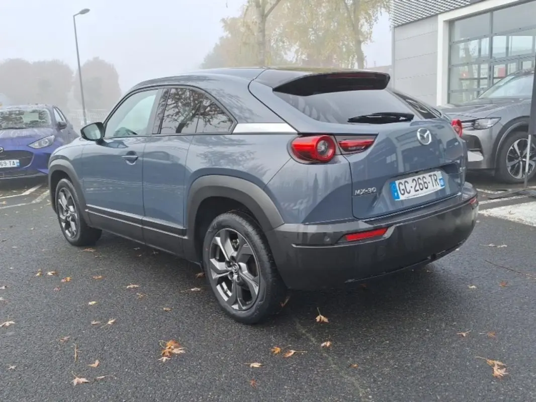 Vue 3/4 arrière droite d'un Mazda MX-30 gris électrique 2021 avec jantes distinctives et feux ronds arrière.