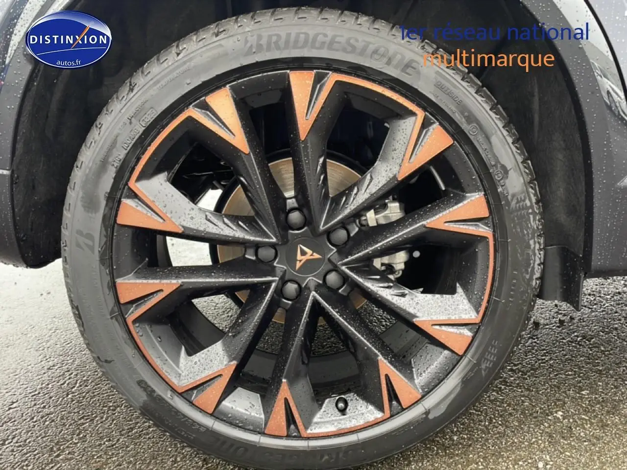 Gros plan sur la jante noire et cuivre du CUPRA Formentor gris graphene, avec pneu Bridgestone sous la pluie.