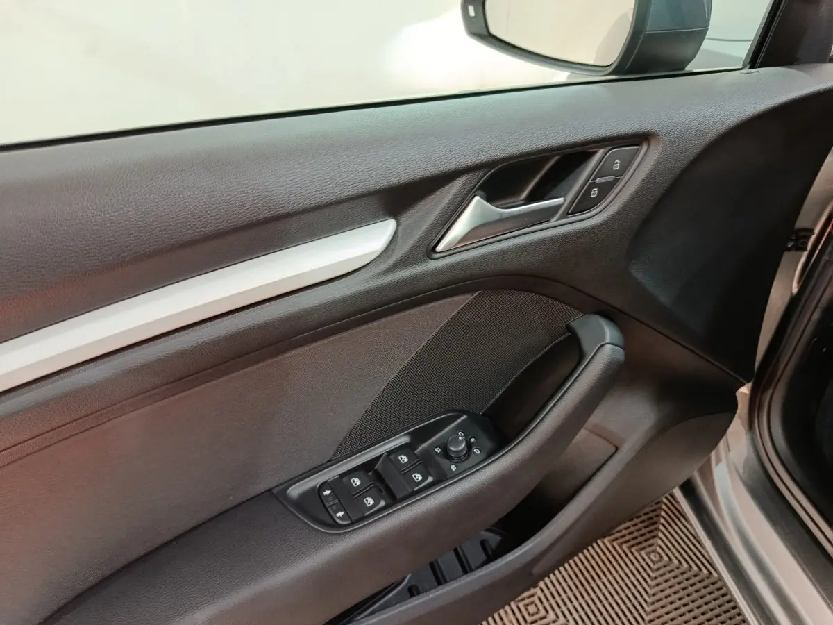 Vue intérieure du panneau de porte avant côté conducteur de l'Audi A3 gris foncé, avec commandes électriques et verrouillage.