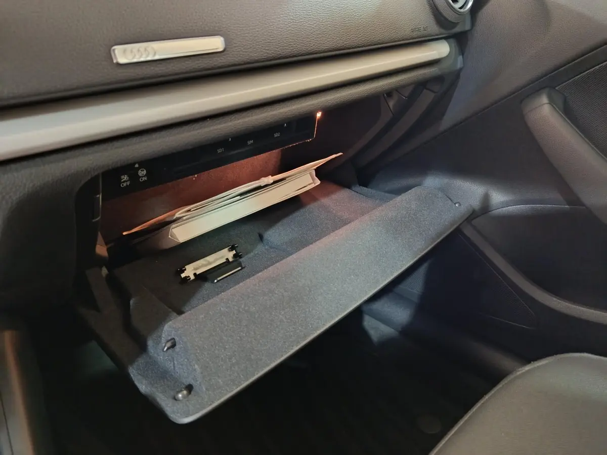 Gros plan sur la boîte à gants ouverte côté passager de l’Audi A3 35 TDI 2020 avec intérieur noir et éclairage intérieur.