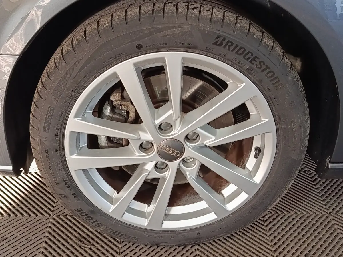 Gros plan sur la roue avant droite d'une Audi A3 gris foncé, jante alliage à plusieurs branches fines.